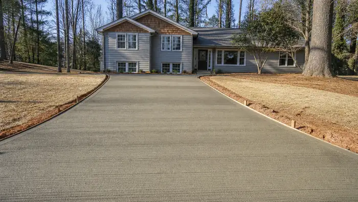 A broom drags across a driveway creating a slip-resistant texture. at a grey split-level home in Marietta, GA, in raking morning side light.