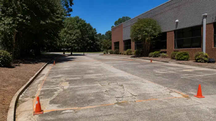 Cracked commercial parking bay marked out for replacement in Marietta, GA, in clear late-morning sun.