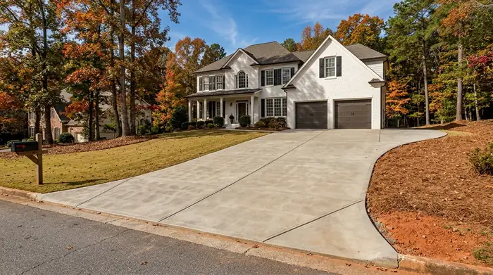 Broom-finished concrete driveway running up to a two-car garage at a painted-white-brick two-story home in Marietta, GA, in clear late-morning sun.