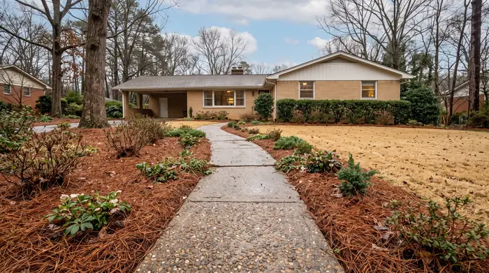 Narrow exposed-aggregate concrete garden path bordered by plantings at a buff-brick ranch home in Marietta, GA, after a rain shower.