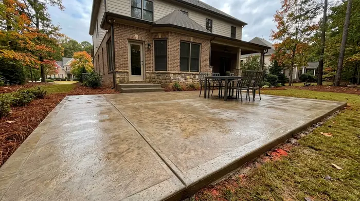 Rectangular concrete patio with a low step up to the rear door at a brick-and-siding two-story home in Marietta, GA, after a rain shower.