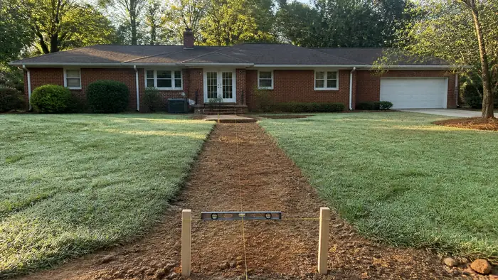 Backyard grade checked with a level and string before a patio pour at a red-brick ranch home in Marietta, GA, in early morning light.