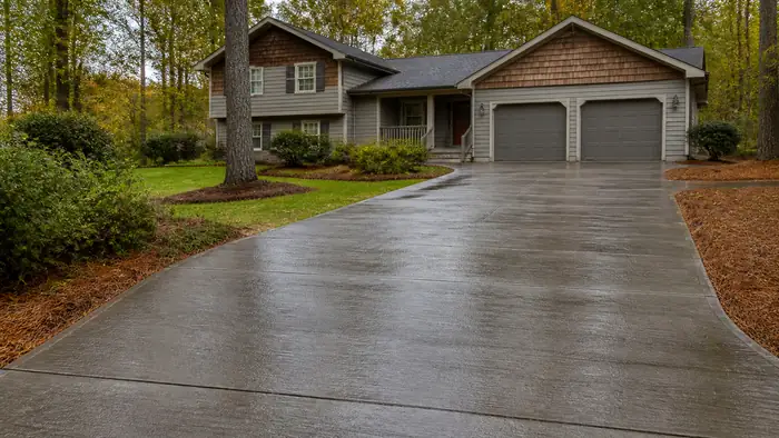 Freshly poured concrete driveway still curing, dark and damp at a grey split-level home in Marietta, GA, after a rain shower.