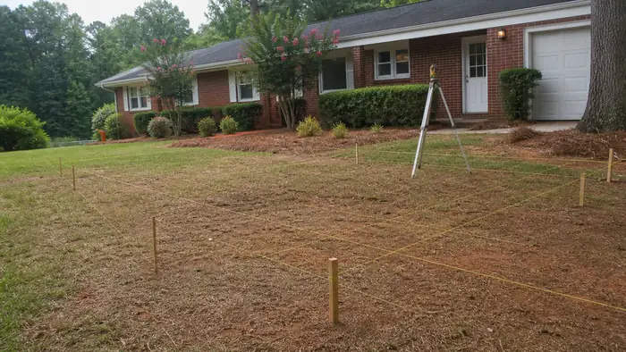 A contractor checks slope and drainage before work begins. at a red-brick ranch home in Marietta, GA, under a hazy afternoon sky.