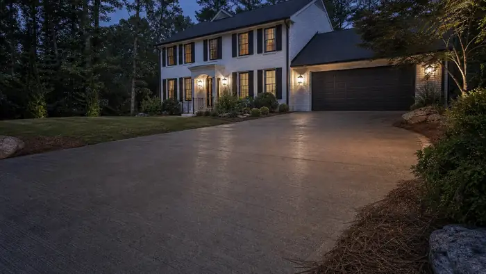 A sprayer applies sealer across a driveway. at a painted-white-brick two-story home in Marietta, GA, at blue hour.